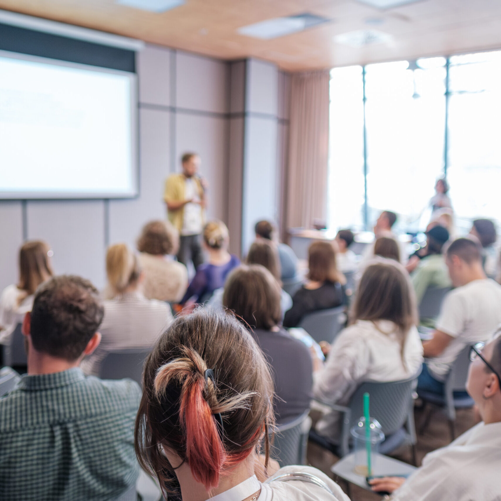 Group of people attending a presentation in a conference room. Speaker giving lecture to engaged audience.
